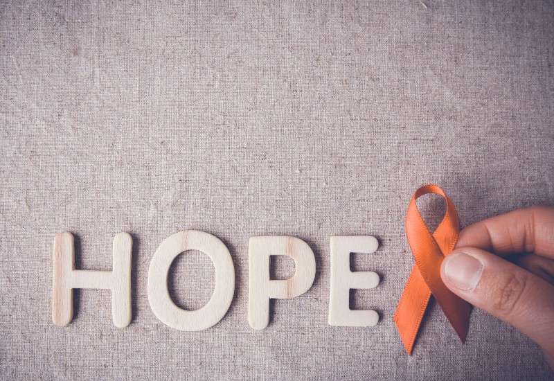 hand holding an orange ribbon next to the word "hope"